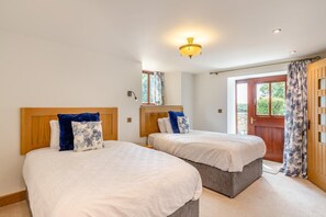A bedroom with two beds, a wooden headboard, a nightstand, a window with curtains, and a door with a view of the outdoors. - 3 Bed in Tremar Coombe (oc-g45783) (Tremar)