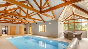 An indoor swimming pool with wooden beams, a seating area with wicker furniture, and a view of the outdoors through large windows. - 3 Bed in Tremar Coombe (oc-g45783) (Tremar)