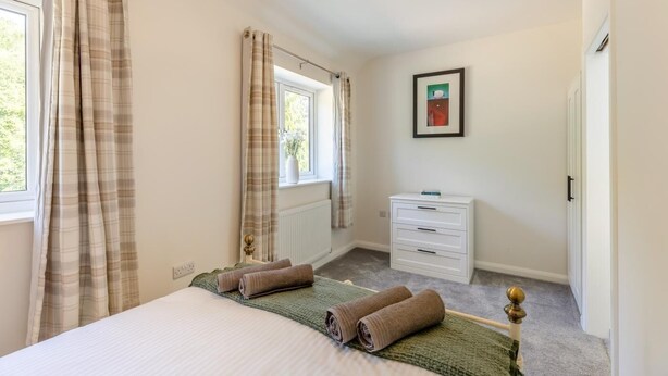 Een slaapkamer met een bed, een dressoir, een radiator, een raam met gordijnen en een lijst met een afbeelding aan de muur.