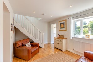A spacious living area with a staircase, a brown leather sofa, a wooden cabinet, and a window with a view of greenery. - 2 Bed in Oreton (oc-h44970) (Oreton)