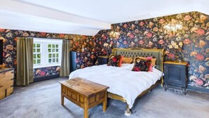 A bedroom with a large bed, floral wallpaper, a wooden nightstand, and a window with curtains. - 4 Bed in Marple (oc-45774) (Marple)
