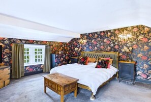 Ein Schlafzimmer mit einem großen Bett, floralem Wandpapier, einem Nachttisch aus Holz und einem Fenster mit Vorhängen.