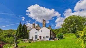 A white building with multiple chimneys, surrounded by lush greenery and a clear blue sky. - 4 Bed in Marple (oc-45774) (Marple)