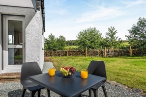 A table with a fruit bowl and two glasses of orange juice, set against a stone wall and a grassy field. - 2 Bed in Tighnabruaich (oc-p45539) (Kilfinan)