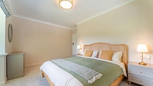 Een slaapkamer met een bed, bedlampen, nachtkastje, dressoir en een spiegel aan de muur.