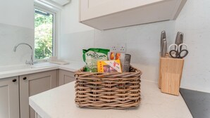 Een keuken met een rieten mand vol boodschappen, een messenblok en een raam met uitzicht op groen.