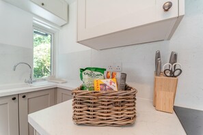A kitchen with a wicker basket containing groceries, a knife block, and a window with a view of greenery. - 2 Bed in Tighnabruaich (oc-p45539) (Kilfinan)