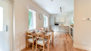 Een moderne keuken met witte kastjes, een magnetron en een spoelbak. Er is een eethoek met houten stoelen en een tafel gedekt voor twee personen.
