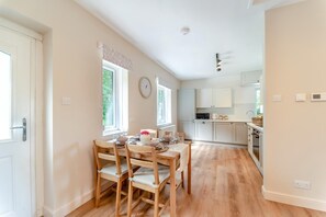 A modern kitchen with white cabinets, a microwave, and a sink. There is a dining area with wooden chairs and a table set for two. - 2 Bed in Tighnabruaich (oc-p45539) (Kilfinan)