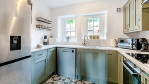 Cocina compacta con refrigerador, lavavajillas y microondas. Dos ventanas aportan luz natural, y el piso presenta un diseño de baldosas con estampado.