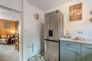 Eine kleine Küche mit einem Kühlschrank, einer Uhr und einem an der Wand befestigten Schild.