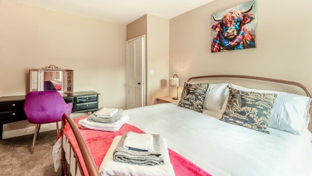 Un dormitorio con cama, una silla, cómoda, espejo y un cuadro en la pared.