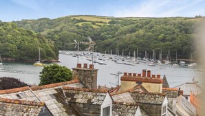 A harbor with numerous boats, surrounded by lush green hills and residential buildings with visible chimneys. - 3 Bed in Fowey (oc-m32343) (Fowey)