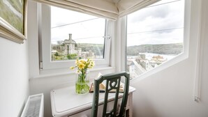 A room with a view of a historic building, a small table with a chair, and a vase with flowers. - 3 Bed in Fowey (oc-m32343) (Fowey)