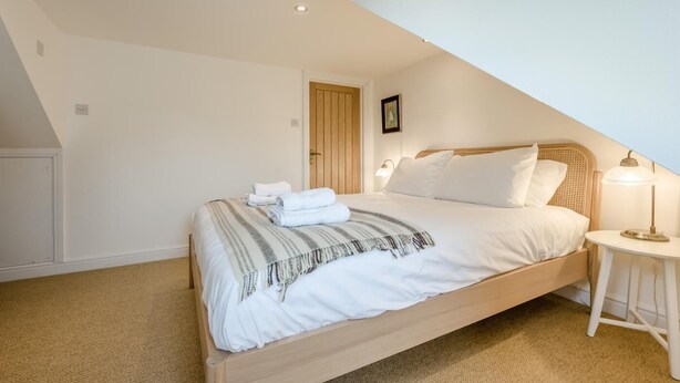 A bedroom with a sloped ceiling, a wooden bed, white bedding, a bedside lamp, and a door with a picture. - 3 Bed in Fowey (oc-m32343) (Fowey)