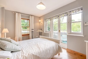 Une chambre à coucher comprenant un lit, une table de chevet, une lampe, une fenêtre avec des rideaux et une vue sur l’extérieur.