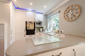 Une cuisine moderne avec des meubles blancs, un four encastré, un four à micro-ondes et une grande horloge murale.