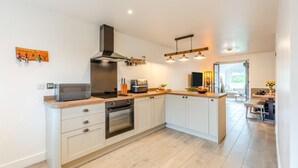 A modern kitchen with a built-in oven, microwave, and a range hood. There is a wooden countertop and a dining area visible in the background. - 2 Bed in Kirkby-in-Furness (oc-s42634) (Kirkby Ireleth)