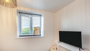 A room with a television on a stand, a window with blinds, and a chair. - 2 Bed in Kirkby-in-Furness (oc-s42634) (Kirkby Ireleth)