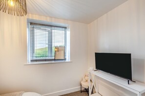 A room with a television on a stand, a window with blinds, and a chair. - 2 Bed in Kirkby-in-Furness (oc-s42634) (Kirkby Ireleth)