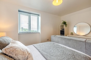 A bedroom with a bed, a bedside table, a mirror, a window with blinds, and a plant. - 2 Bed in Kirkby-in-Furness (oc-s42634) (Kirkby Ireleth)