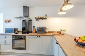 A modern kitchen with a built-in oven, a microwave, a toaster, a range hood, and a wooden countertop. - 2 Bed in Kirkby-in-Furness (oc-s42634) (Kirkby Ireleth)