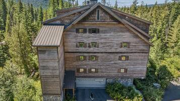 Une cabane en rondins à deux étages, avec des fondations en pierre, entourée d’une forêt dense et de montagnes.