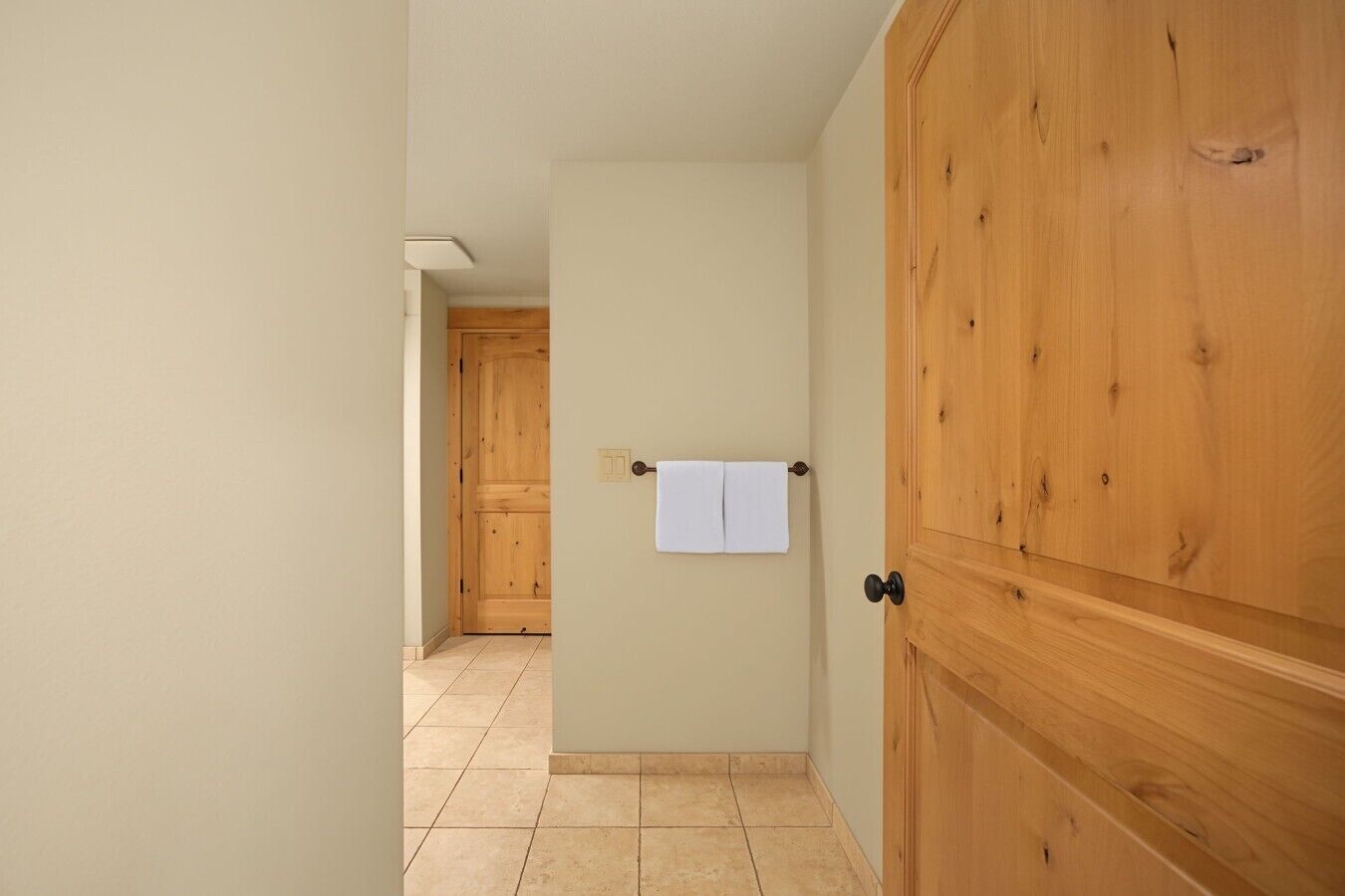 A hallway with a wooden door, a towel hanging on the wall, and a tiled floor.