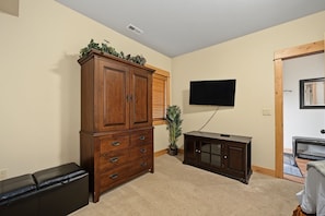 A living room with a wooden cabinet, a television, a small plant, and a sofa.