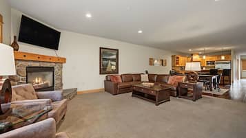 A living room with a stone fireplace, a large flat-screen TV, a sectional sofa, and a dining area with wooden cabinets.