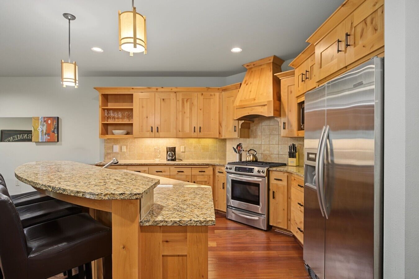 A modern kitchen with wooden cabinets, a granite countertop, stainless steel appliances, and pendant lighting.