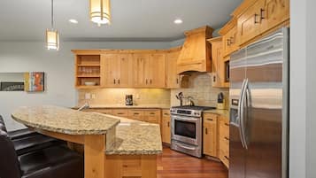 A modern kitchen with wooden cabinets, a granite countertop, stainless steel appliances, and pendant lighting.
