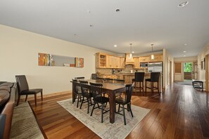 A spacious living area with a dining table, chairs, a sofa, and a kitchen in the background.