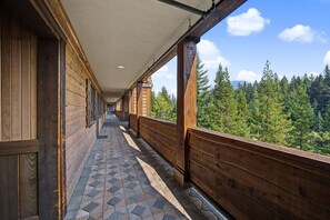 A corridor with wooden walls and a tiled floor leading to a balcony with a view of a forest.