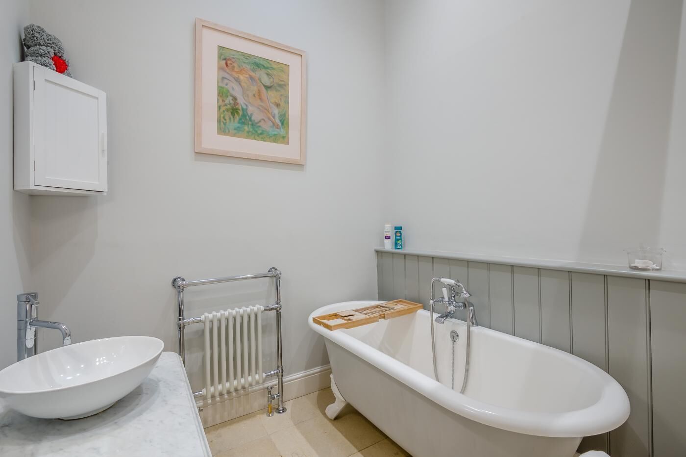 A bathroom with a freestanding bathtub, a white sink, a towel rack, and a framed painting on the wall.