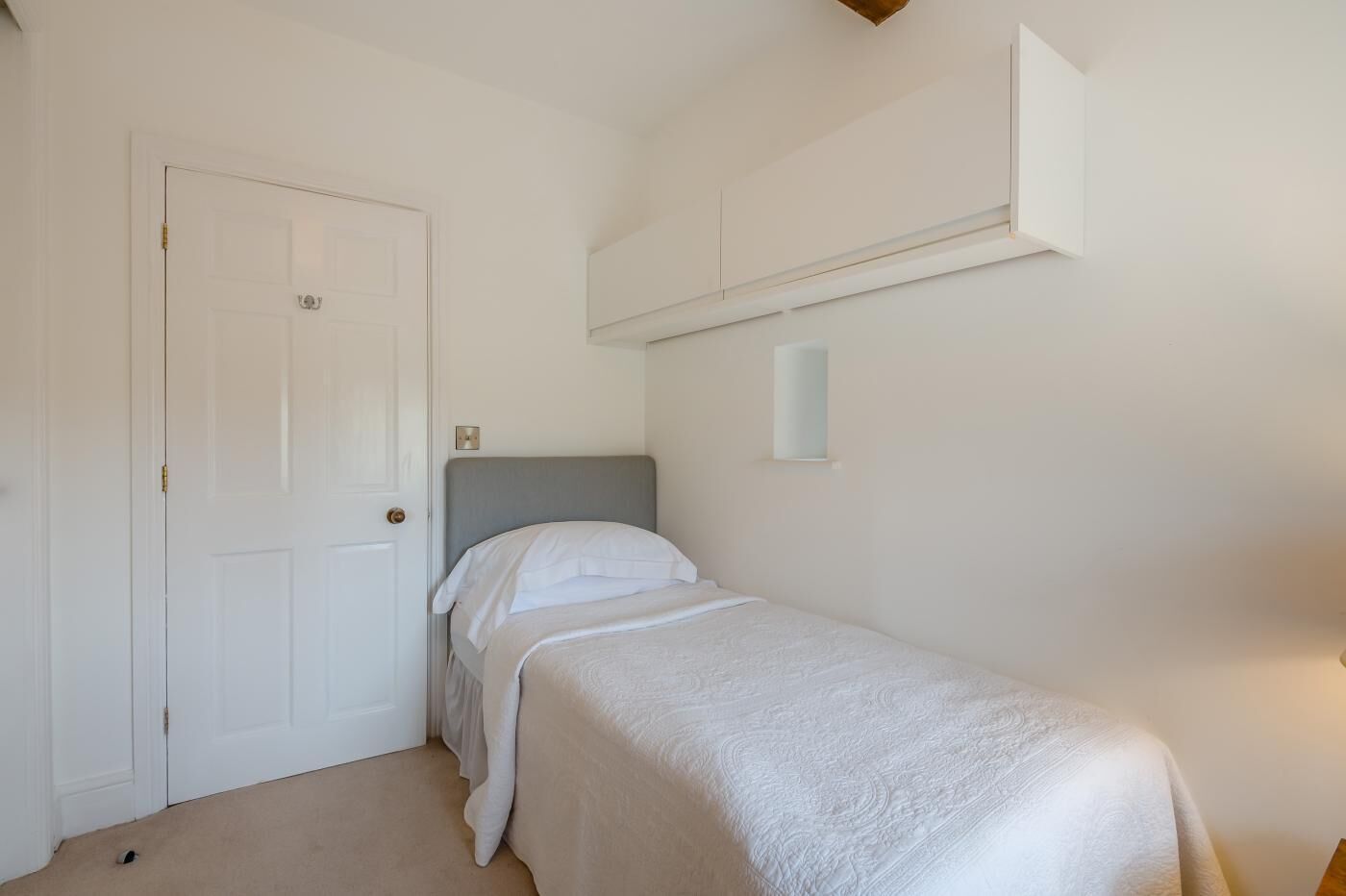 A single bed with a grey headboard in a room with white walls and a white door.