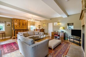 A living room with a sofa, coffee table, and a television. There is a fireplace with a mantel and a chandelier. - 4 Bed in Wensley (oc-t45784) (Wensley)
