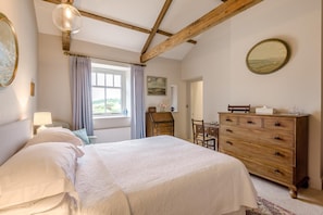 Quarto com uma cama grande, cómoda de madeira e janela com cortinas.