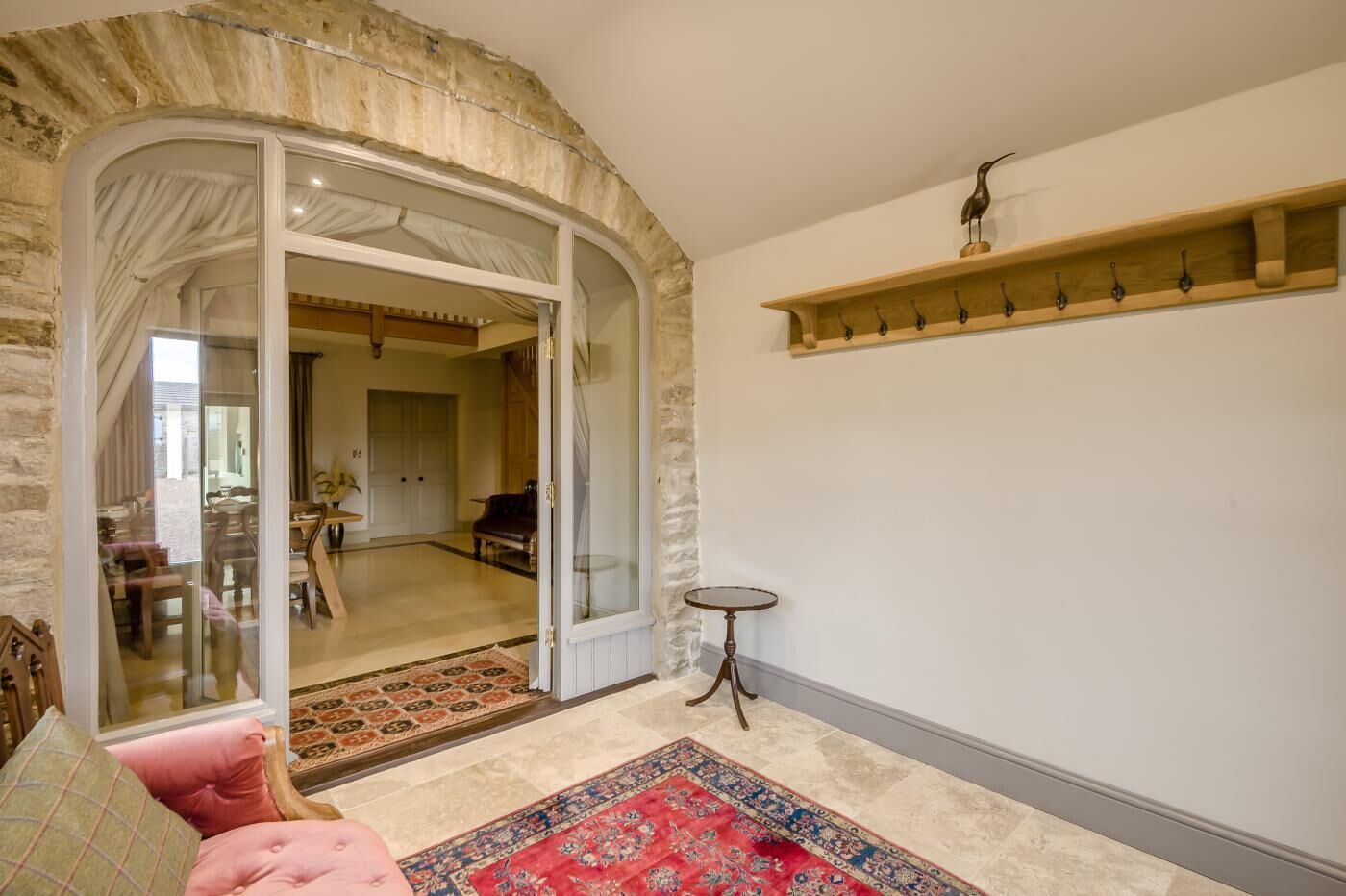 A room with a stone archway leading to a dining area, a red patterned rug, and a wooden shelf with hooks.