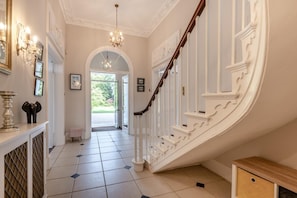 A grand staircase with white balustrades and a chandelier, leading to an open doorway. - 6 Bed in West Malling (oc-n45282) (Kings Hill)