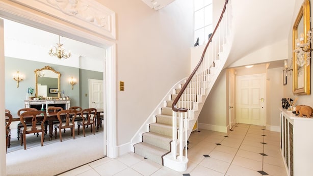 A spacious foyer with a grand staircase, a dining area with wooden chairs, and a fireplace. - 6 Bed in West Malling (oc-n45282) (Kings Hill)