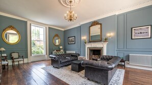 A room with a fireplace, leather sofas, a chandelier, and a large mirror. - 6 Bed in West Malling (oc-n45282) (Kings Hill)