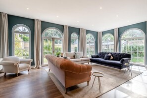 Un salón amplio con un ventanal grande, un sofá marrón, un sofá oscuro y un sillón blanco.