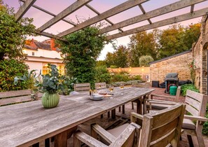 Un patio al aire libre con una mesa de madera, sillas y una estructura de pérgola.