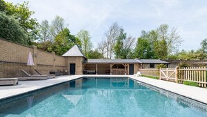 A rectangular swimming pool with a brick wall and a covered seating area. - 6 Bed in West Malling (oc-n45282) (Kings Hill)