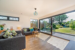 Ein modernes Wohnzimmer mit grauem Sofa, einem Couchtisch und einer großen Schiebeglasdoor, die in einen Garten führt.