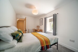 Ein Schlafzimmer mit Bett, Schreibtisch, Stuhl, einem Fenster mit Vorhängen und einer Hängelampe.