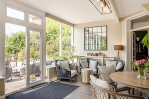 A spacious room with a large sliding glass door leading to a patio area, furnished with wicker chairs and a round table.