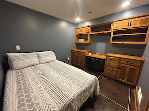A bedroom with a bed, wooden cabinets, and a built-in desk.