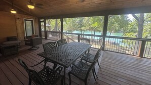 A covered outdoor deck with a table and chairs, a ceiling fan, and a view of a body of water. - Charming Modern Craftsman Right on the Water (Linn Valley)